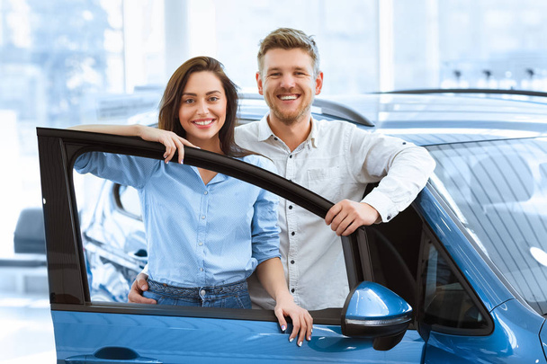 Perfecte gezinsauto. Shot van een mooie gelukkige paar poseren samen achter een open deur voor een nieuwe auto die ze net gekocht bij de dealer glimlachen naar de camera vreugdevol - Foto, afbeelding