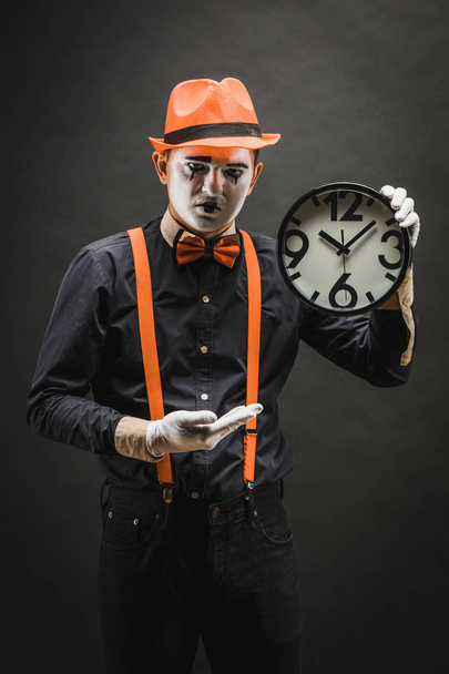 Gruselige Clown-Pantomime mit Uhr in den Händen, auf dunklem Hintergrund. - Foto, Bild
