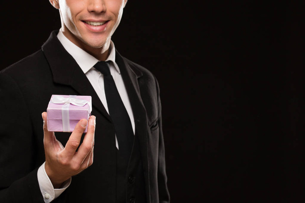 Cropped shot of an attractive suited man holding out a gift with a bow to the camera smiling seductively on black background copyspace love romance relationships dating valentines surprise - Photo, Image