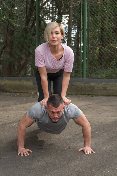 A muscular man push-ups during training with a girl on his back - Foto, afbeelding