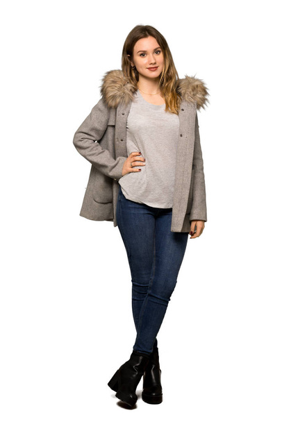 A full-length shot of a Teenager girl with coat posing with arms at hip and smiling on isolated white background - Photo, Image