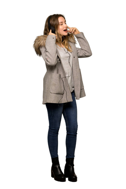 Полнометражный снимок девочки-подростка в пальто, слушающей музыку в наушниках на изолированном белом фоне
 - Фото, изображение