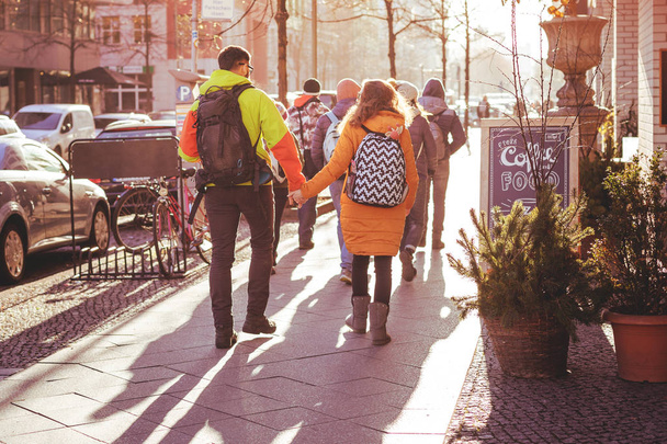 若い人たちのグループは、冬のベルリンの街を歩きます。いくつかのカップルは、手を握り合います。明るい太陽の下でバックライトで撮影します。2018 年 12 月. - 写真・画像