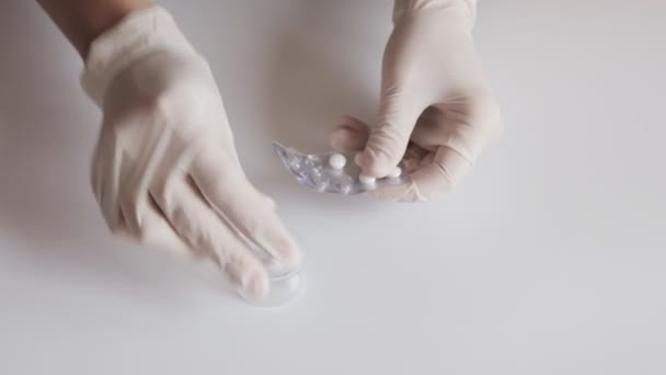 A nurse in white latex gloves squeezes tablets out of the blister on white table - Filmati, video