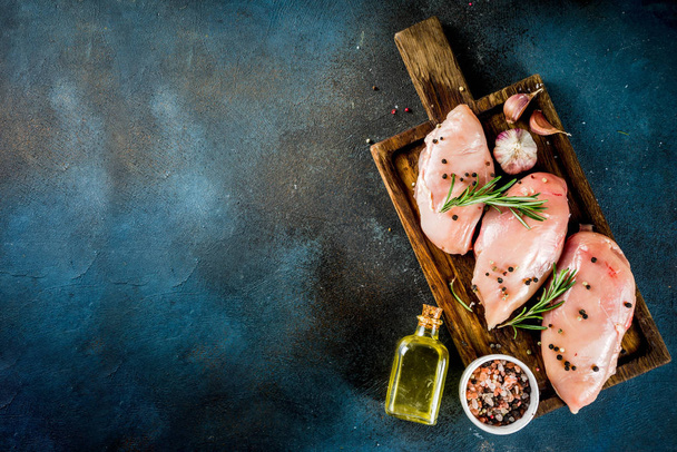 Raw fresh chicken breast fillet with spices and rosemary on a dark blue concrete background, top view with copy space for text - Zdjęcie, obraz