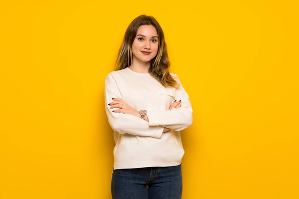 Chica adolescente sobre pared amarilla manteniendo los brazos cruzados en posición frontal
 - Foto, imagen