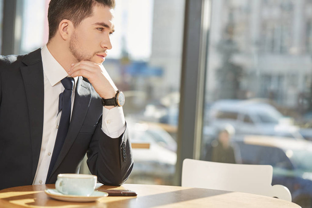 Бізнес-рішення. Обрізаний знімок гарного бородатого бізнесмена, який задумливо дивиться, маючи чашку кави в кав'ярні
 - Фото, зображення
