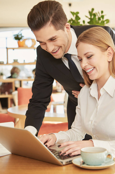 Hasznos partner. Jóképű üzletember Wesola segít mosolygó női kollégája dokumentumokat a laptop ebéd az étteremben - Fotó, kép
