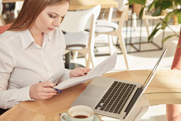 Letzter Check. vertikale Aufnahme einer schönen Geschäftsfrau, die während ihrer Kaffeepause im örtlichen Restaurant mit Papieren arbeitet   - Foto, Bild