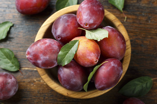 ripe red plum in a plate on a shabby wooden background. place for text - Foto, Imagem