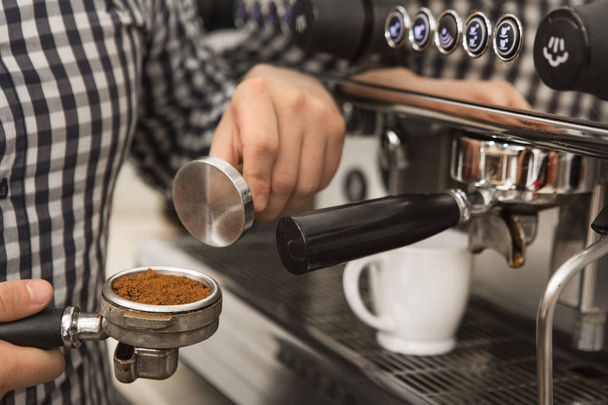 Schnappschuss eines professionellen Baristas, der in der Nähe einer Kaffeemaschine in seinem Café steht und Kaffee zubereitet, hält einen Stampfer und Filter mit gepresstem Kaffee in der Hand Beruf Hipster-Arbeiter-Job - Foto, Bild