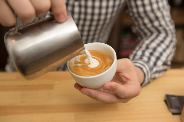 Nahaufnahme eines professionellen Baristas, der Kaffeekunst macht, indem er Milch in Kaffee gießt und heiße köstliche Getränke für seinen Kundendienst zubereitet Professionalität Kreativität Beruf Hipster-Konzept - Foto, Bild
