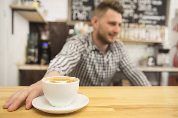Selective focus on a cup of fresh coffee barista working at his coffee shop on the background copyspace profession occupation job entrepreneur owner startup small business businessman casual hipster - Foto, imagen