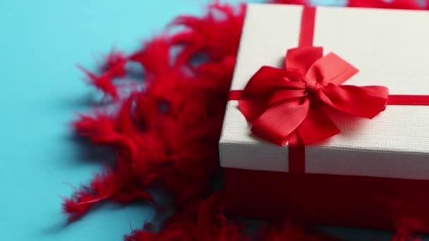 Box with a gift, tied with a ribbon placed on red feathers - Footage, Video