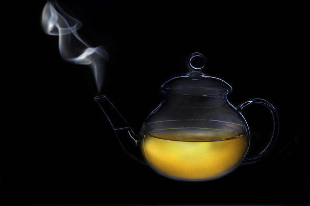 one object on a black background, a glass transparent teapot with tea, steam comes out of the spout - Foto, Bild