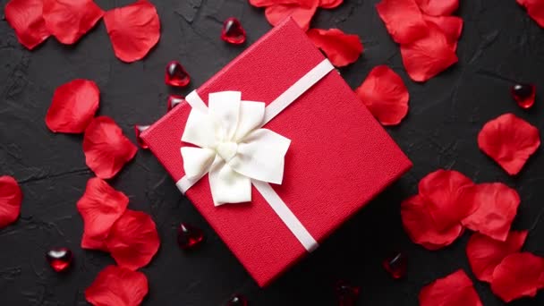 Gift box on black stone table. Romantic holiday background with rose petals - Footage, Video