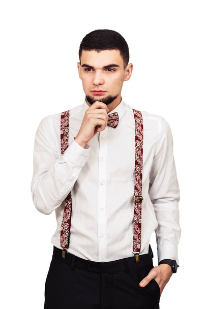 Stylový mladý vousatý muž v košili, kalhoty a šle pózuje na bílém pozadí - Fotografie, Obrázek