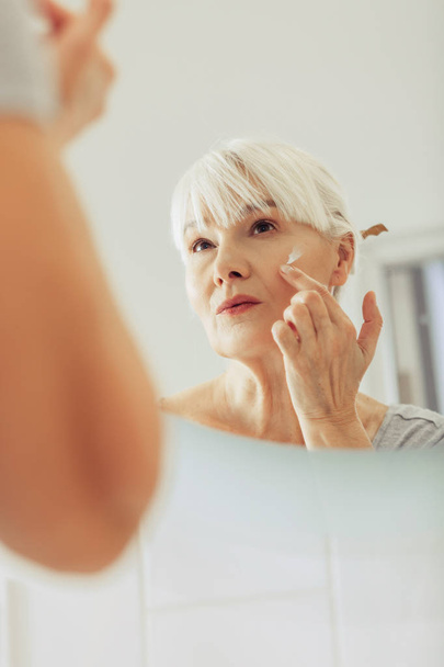 Pleasant nice woman applying cream on her face - Fotoğraf, Görsel