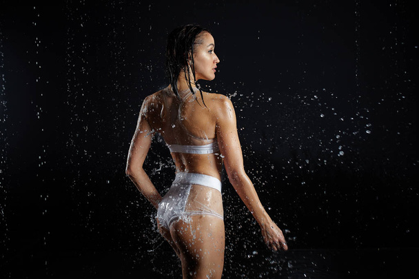 Beautiful young girl in sportswear poses in aqua studio. Drops of water spread about her fitness body. The perfect figure on the background of water splashes - Zdjęcie, obraz
