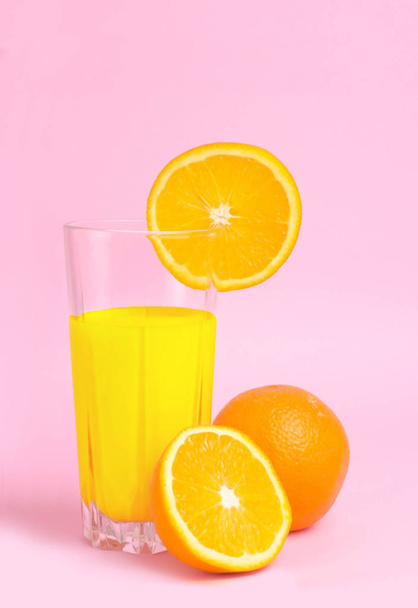 A glass with orange juice with the cut oranges on a pink background. Juicy color scale, pin up, pop up styles. Food for breakfast, a healthy drink with vitamins and miniroalami. A sunny drink. Fruit. - Photo, Image