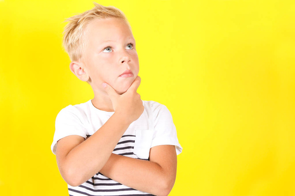 Cute blond boy portrait dreaming of something on yellow background - Photo, Image