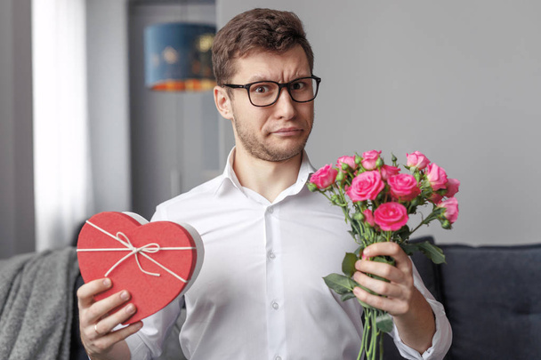 Homem descontente com o presente do Dia dos Namorados e flores
 - Foto, Imagem