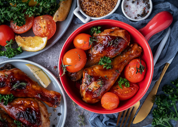 baked chicken legs in a barbecue sauce with tomatoes in a red frying pan, top view - Foto, Imagem