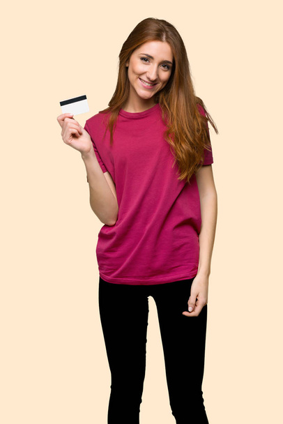 Menina ruiva segurando um cartão de crédito no fundo amarelo isolado
 - Foto, Imagem