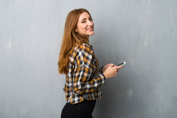 Молода руда дівчина над гранжевою стіною надсилає повідомлення з мобільним
 - Фото, зображення