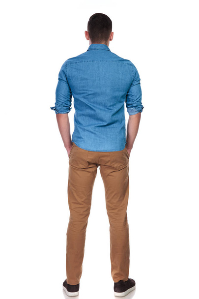 back view of young and relaxed casual man standing on white background with hands in pockets, full length picture - Photo, Image