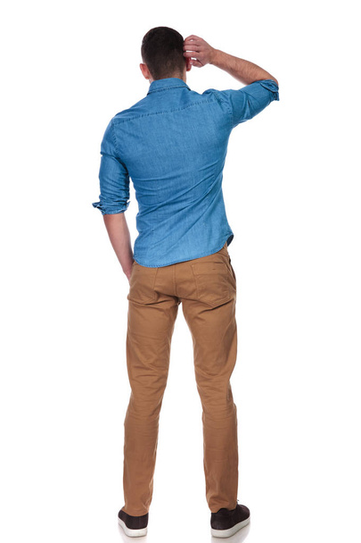 rear view of curious casual man waiting with hand in pocket on white background, full body picture - Foto, imagen