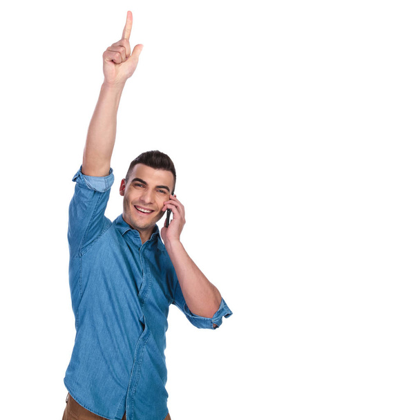glücklicher lässiger Mann telefoniert und zeigt mit dem Finger nach oben, während er auf weißem Hintergrund steht, Porträtbild - Foto, Bild