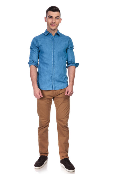 young and handsome man wearing blue shirt standing on white background with rolled sleeves, full body picture - 写真・画像
