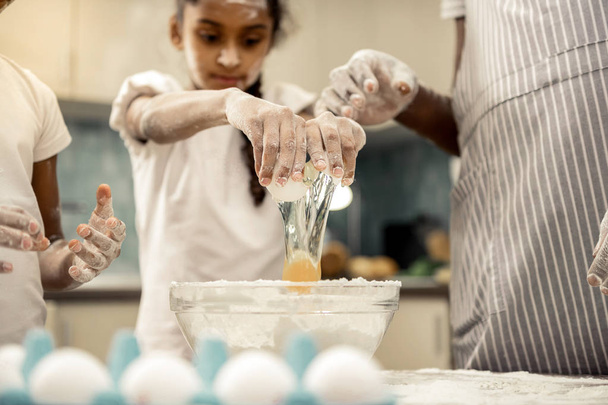 Cute dark-haired daughter beating egg cooking with father - Valokuva, kuva