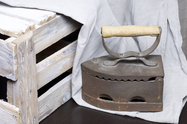 Old iron, heated by hot coals. Standing next to a wooden box and linen cloth. - Фото, зображення
