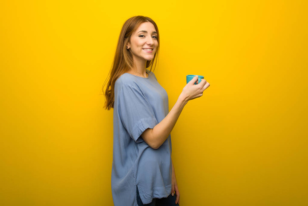 Chica pelirroja joven sobre fondo amarillo de la pared sosteniendo una taza de café caliente
 - Foto, imagen