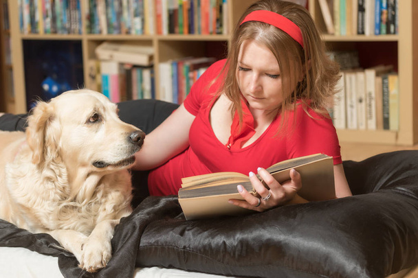 Cool attractive young woman in red is reading a book and her dog is looking at her.  - Photo, Image