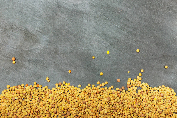 Raw lentils on balck stone background. Healthy vegetarian food concept. Superfoods. Top view, copy space. Lentils are rich in complex carbohydrates, fiber, high in protein and make an excellent meat alternative. - Фото, изображение