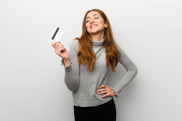 Redhead girl over white wall holding a credit card and thinking - Foto, imagen