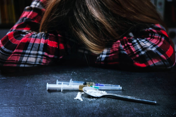 Jonge vrouw en spuit met heroïne of cocaïne op tafel, selectieve aandacht - Foto, afbeelding