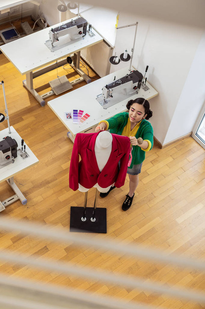 Brunette asian designer in a short skirt putting a jacket on a dummy - Photo, image