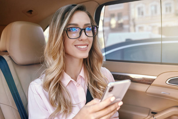 attractive businesswoman holding smartphone and looking away in the car - 写真・画像