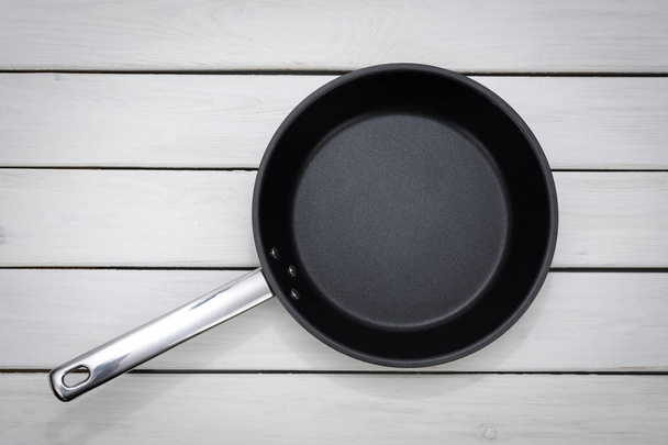 Μαγειρικό πρότυπο - θέα πάνω του ένα άδειο τηγάνι σε φόντο λευκό ξύλινη σανίδα.  - Φωτογραφία, εικόνα