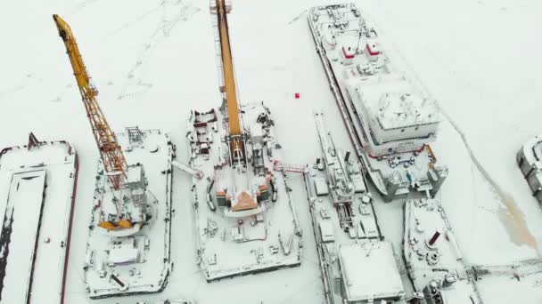 frozen seaport, winter berths of ships, ice-bound tankers, simple cranes of the shipyard, aerial view, aerial survey, copter shoot - Materiał filmowy, wideo