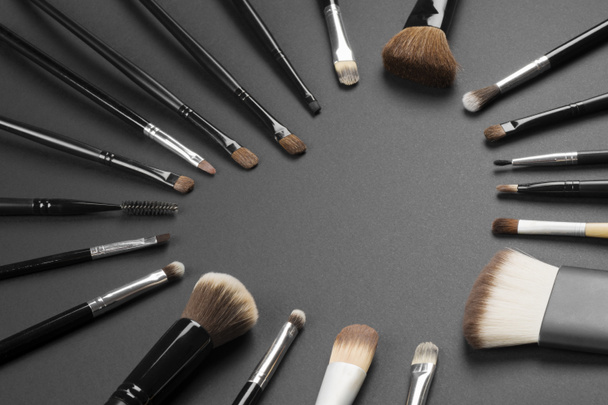 Different make-up brushes are in heart shape on gray background, loving make-up concept. - Photo, Image