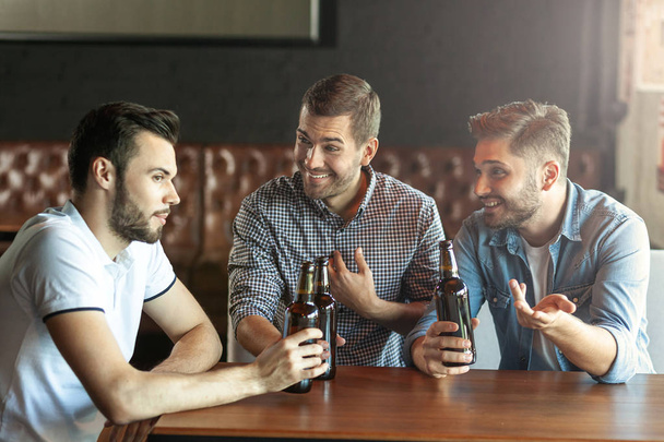 three friends talking together while drinking beer in cafe - Zdjęcie, obraz