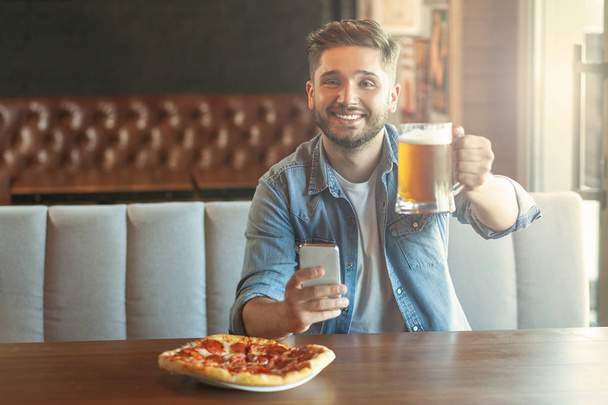 portrait of smiling man holding glass of beer in cafe and looking at the camera - Foto, imagen