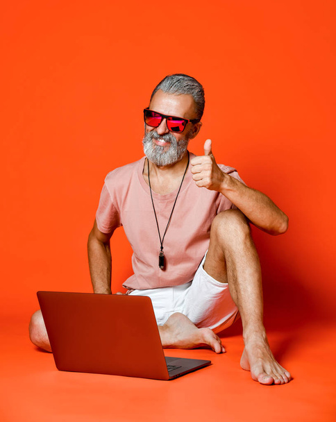 Full length portrait of a happy old man using laptop computer isolated over orange background - Zdjęcie, obraz