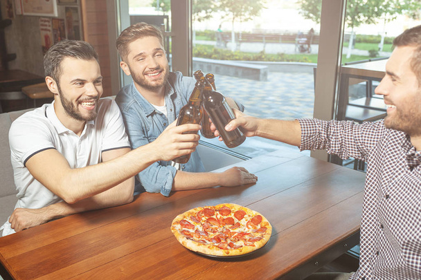 men drinking beer together and eating pizza in cafe - 写真・画像
