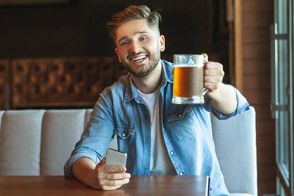 front view of man holding up glass of beer in cafe - Photo, Image